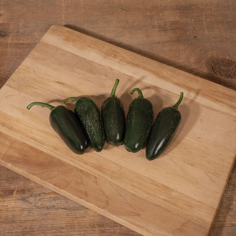 Dark green Black Magic jalapeño peppers on a wooden cutting board